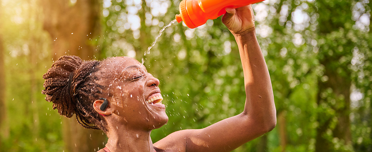 Mulher se refrescando derramando água sobre a cabeça enquanto usa os fones de ouvido esportivos Philips ao ar livre